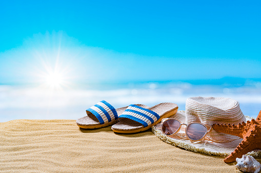 Summer accessories: sandals, sun hat and sunglasses on gold colored sand dune. The composition is at the right of an horizontal frame leaving useful copy space for text and/or logo at the left. High resolution 42Mp outdoors digital capture taken with SONY A7rII and Zeiss Batis 40mm F2.0 CF lens