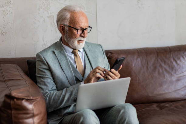 istock Senior man sitting in a lobby, using his phone 1395697412