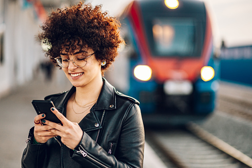 Tourist woman texting message and plan route of stop railway and railroad transport. Enjoying travel concept. Girl texting on smartphone while at the train station and the train is arriving.