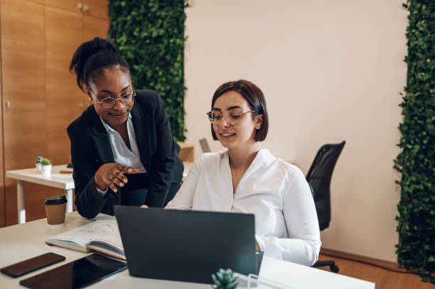 istock Woman executives at work discussing marketing report while using laptop during a meeting in the office. Hardworking young female entrepreneurs. 1395698573