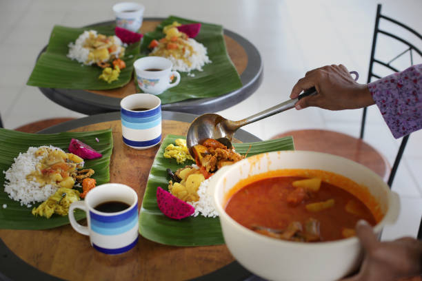 A plated meal featuring a savory stew or sauce in a white bowl, accompanied by sliced potatoes (likely fried or roasted), and mixed vegetables, possibly including green beans. A tomato garnish and rosemary sprig add visual appeal. The setting suggests restaurant dining or a carefully prepared home-cooked meal. The image represents food presentation, culinary arts, and a balanced, appetizing dish.