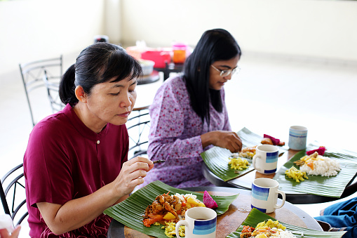 Asian women are enjoying banana leaf rice during lunch potluck session.