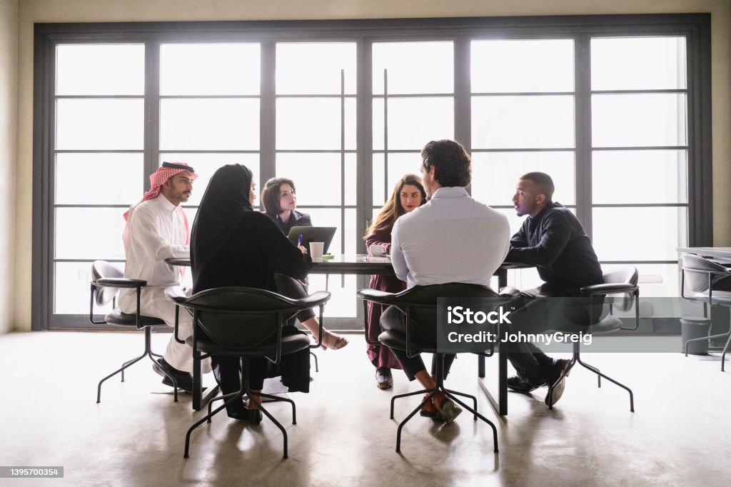 Middle Eastern businesspeople discussing project plans Full length view of six young male and female associates in traditional and western attire sharing objectives and goals. Saudi Arabia Stock Photo