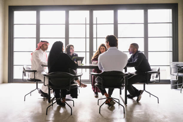 Middle Eastern businesspeople discussing project plans Full length view of six young male and female associates in traditional and western attire sharing objectives and goals. saudi arabia stock pictures, royalty-free photos & images