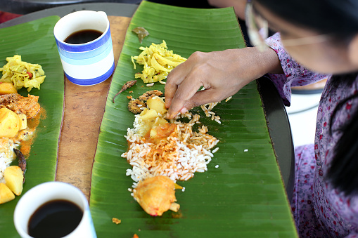 An Asian woman is enjoying banana leaf rice during lunch potluck session.