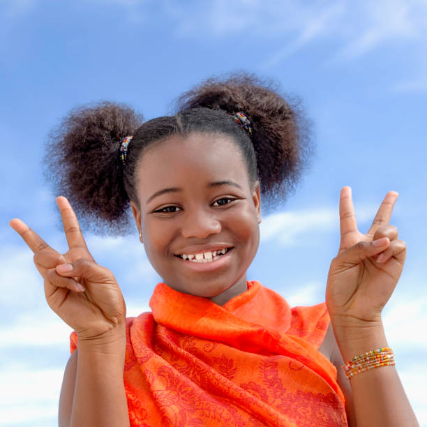 pretty girl with pigtails smiling and showing a victory sign, ten years old, blue sky, white clouds, outdoor portrait, photo - 10 11 years cheerful happiness fun imagens e fotografias de stock