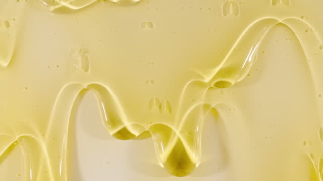 Yellow Transparent Cosmetic Gel Fluid With Molecule Bubbles Flowing On The Plain White Surface. Macro Shot of Natural Organic Cosmetics, Medicine. Production Close-up. Slow Motion