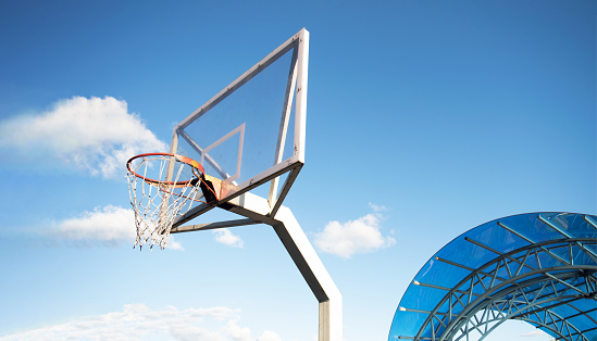 Side view of a basketball hoop with a backboard on a sports field, against a blue sky. Achievement, sports concept