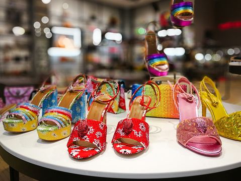 Selective focus color image depicting an arrangement of colorful, sparkly high heels on display in a luxury shoe store.