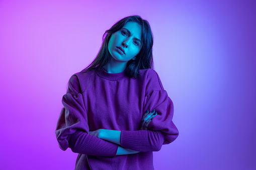 Looks sad. Studio shot of young attractive girl, student with long hair isolated over purple studio background in neon light. Concept of youth, fashion, emotions, vision and facial expression.