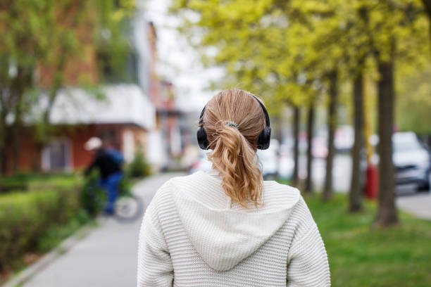 woman with wireless headphones walking on city street - back alley audio imagens e fotografias de stock