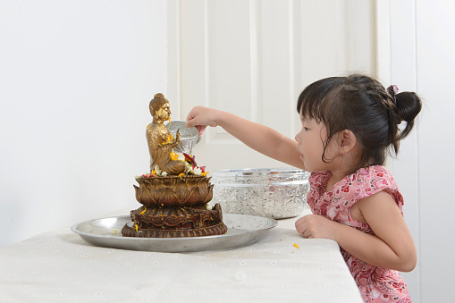 Cute Asian girl bathing Buddha statue for blessings in Songkran tradition in Thailand.