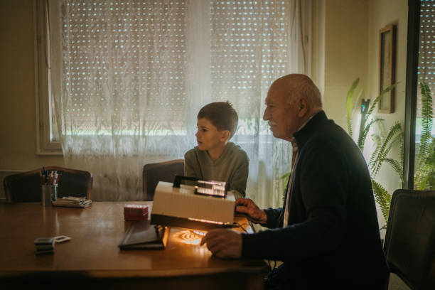 Grandfather and grandson Grandfather and grandson sitting at the table and looking photos on vintage slide projector at elderly man's home. slide projector photos stock pictures, royalty-free photos & images