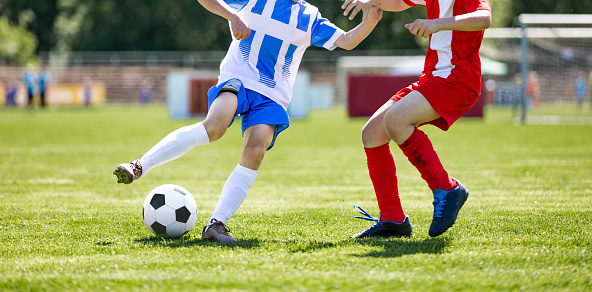 Boys play soccer. Teenagers at school playing soccer in sports field. Children kicking soccer game outdoors. Young male footballers running in red and blue sports uniforms