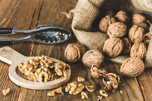 Whole and peeled walnuts on a rustic wooden table, focus on the walnut kernels
