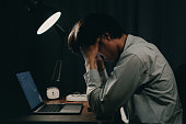 man holding his head in front of a study desk laptop