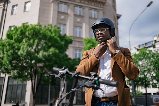 Young adult male entrepreneur strapping on his helmet before proceeding with his commute through the city on his electric bicycle