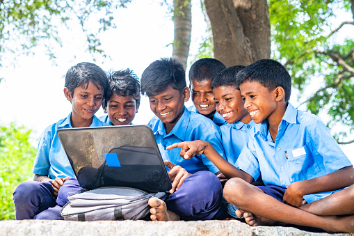 Village group of kids in uniform with using laptop while sitting on near paddy field - concept of education, development and technology