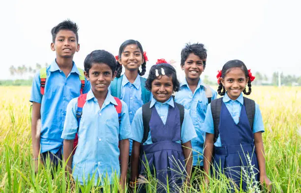 Photo of group of happy smiling village school kids in uniform standing at middle paddy field by looking camera - concept of friendship, education and togetherness