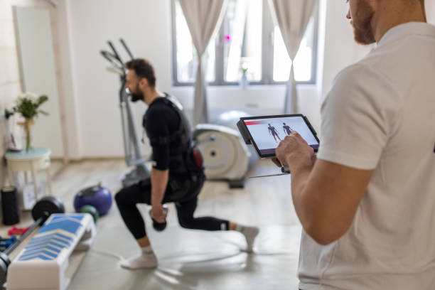 istock Fitness trainer controlling EMS suit using digital tablet while young man exercising 1395728754