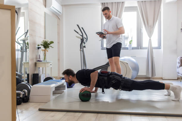 istock Fitness trainer controlling EMS suit using digital tablet while young man exercising 1395729119
