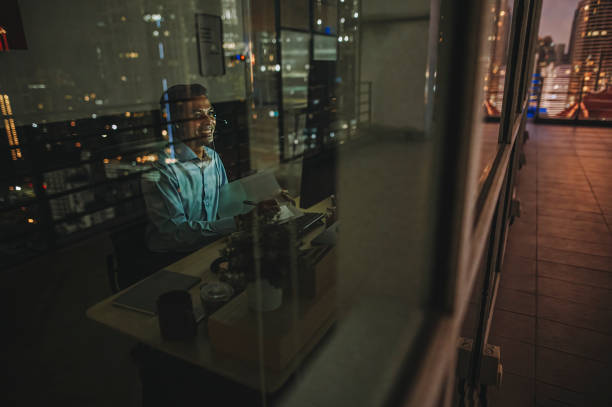 istock Asian Indian male white collar worker video call working late in office alone in low light 1395732148