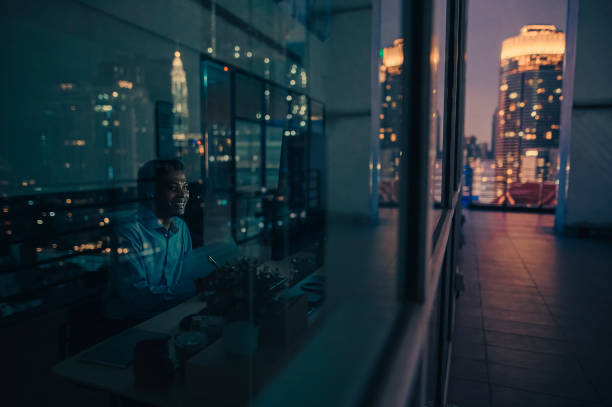 videollamada de trabajador de cuello blanco indio asiático que trabaja hasta tarde en la oficina solo con poca luz - night cityscape reflection usa fotografías e imágenes de stock