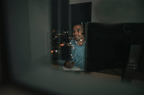 istock Asian Indian male white collar worker video call working late in office alone in low light 1395732169