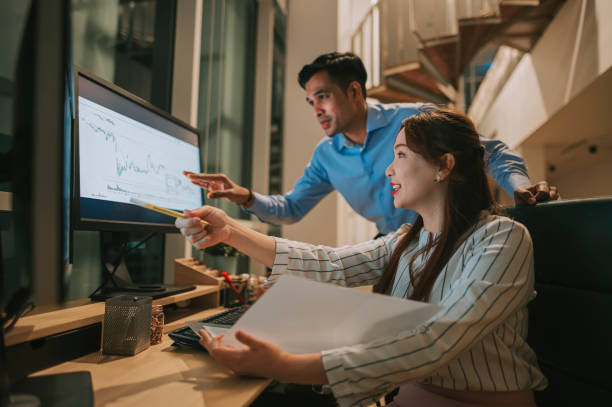 istock Asian colleague working late at night in office with multiple screen 1395732197