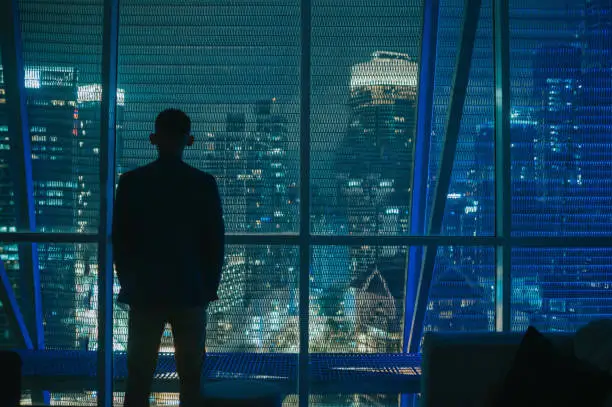 Asian Chinese businessman in silhouette rear view looking at city at night with blue illuminated city light