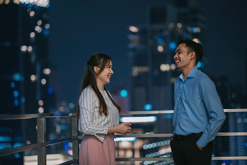 Asian colleague talking in balcony corridor outside office building at night after work