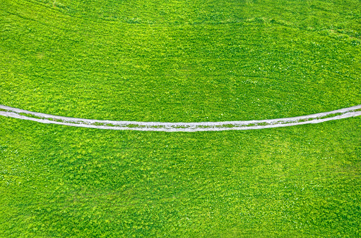 Unpaved countryside road across green field, drone view from above