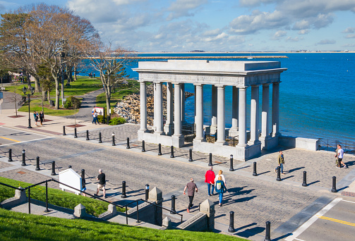 Plymouth, Massachusetts, USA- May  1, 2022- A group of tourists cross a street to get to  the columned memorial housing the rock where pilgrims supposedly first stepped foot onto a new colony in 1620.  The monument was erected on the 300th anniversary of the event.