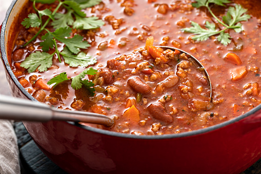 Traditional chili soup with meat, vegetables and red beans in a dutch oven with a ladle