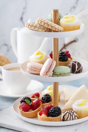 Spring or summer dessert table, three tiered tray with variety of desserts and sandwiches for tea