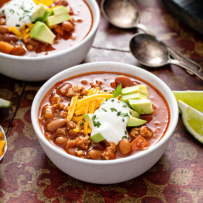 Traditional chili soup with meat, vegetables and red beans in white bowls with all the toppings