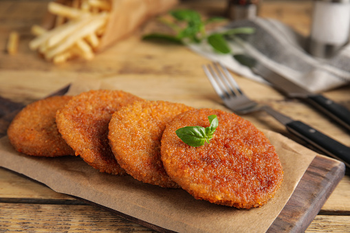 Delicious fried breaded cutlets with basil on wooden table