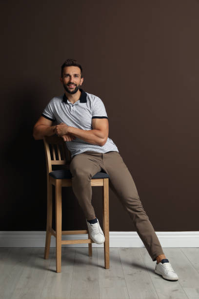 istock Handsome man sitting on stool near brown wall 1395742240