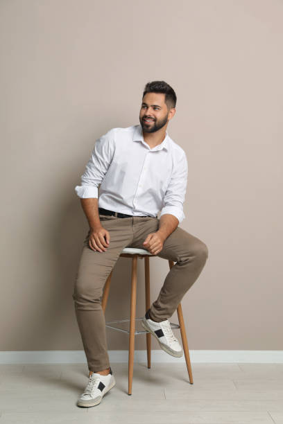 istock Handsome young man sitting on stool near beige wall 1395742243