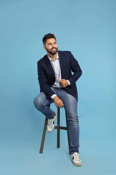 istock Handsome young man sitting on stool against turquoise background 1395742275