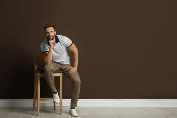 istock Handsome man sitting on stool near brown wall. Space for text 1395742277