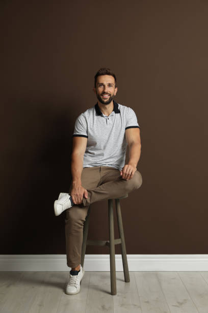 Handsome man sitting on stool near brown wall