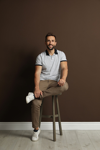 Teenag guy sitting on a white column and smiling at camera isolated on white background