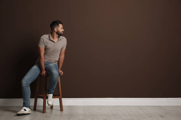 istock Handsome young man sitting on stool near brown wall. Space for text 1395742819