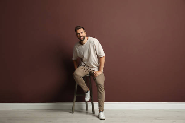 istock Handsome man sitting on stool near brown wall 1395742822