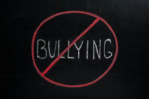 Photo of Prohibition sign with word Bullying chalked on blackboard