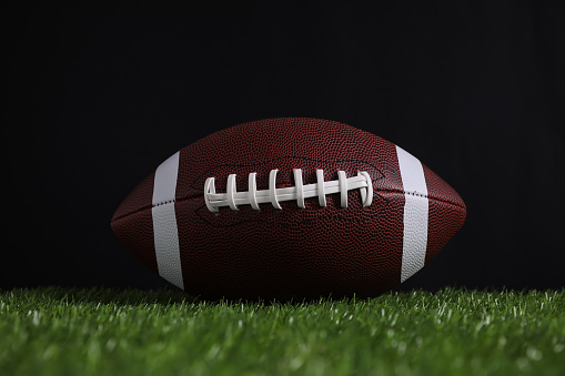 American football ball on green grass against black background