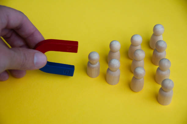 istock Hand holding magnet attracting wooden dolls on yellow background. 1395745945