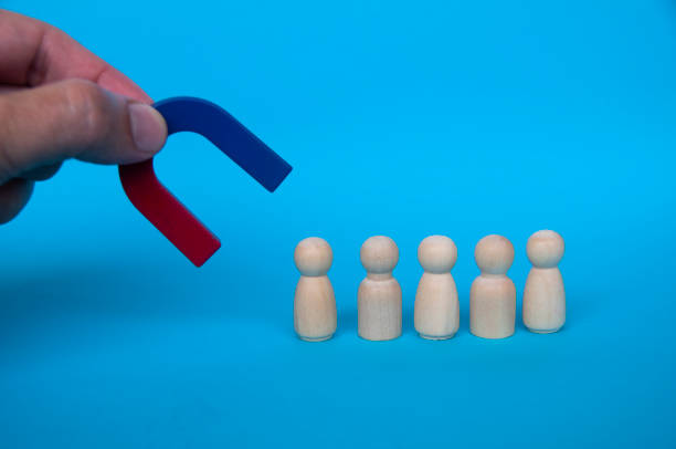 istock Hand holding magnet attracting wooden dolls on blue background. 1395745960