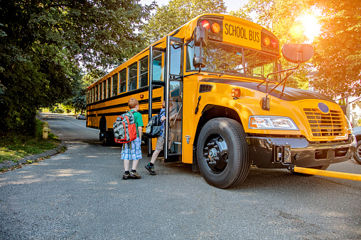 Un niño subiendo a un autobús escolar bajo el sol photo